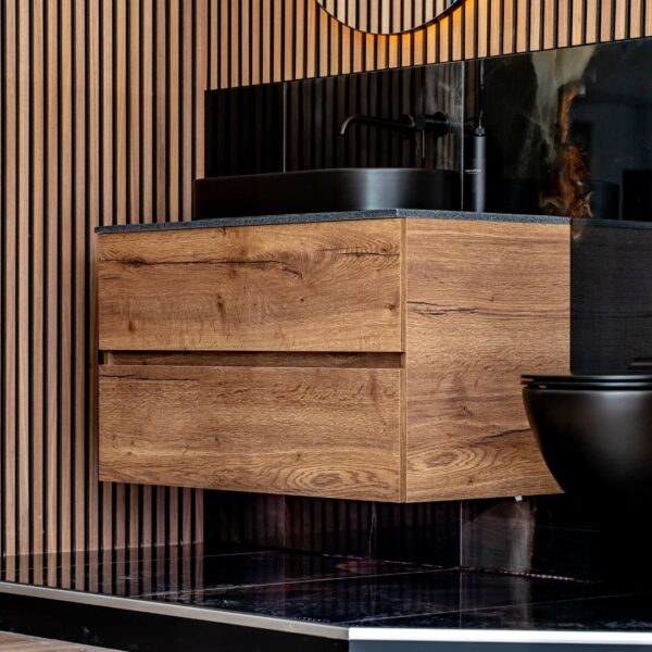 A modern, dark wood floating vanity with a black sink and faucet. The bathroom features vertical wood paneling and black marble-style tile.