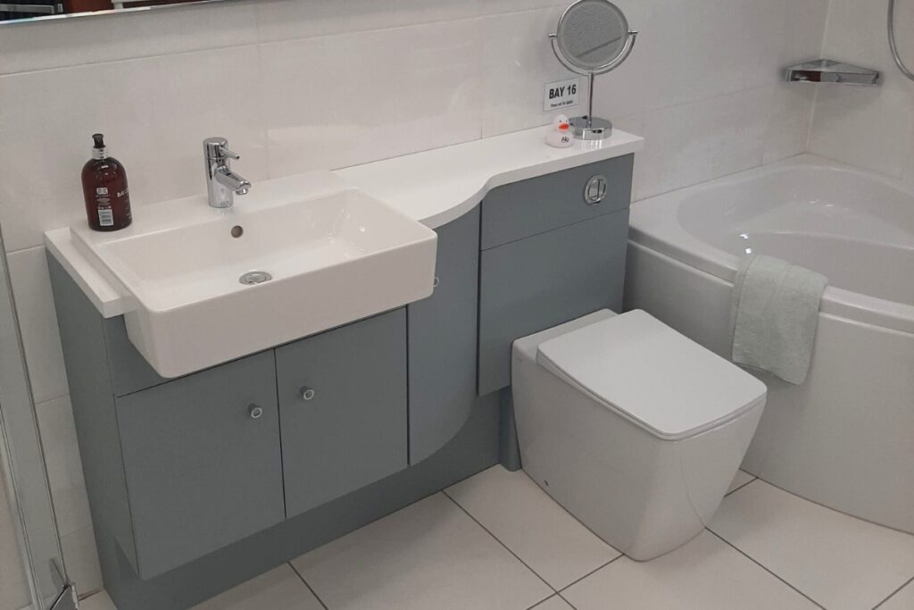 A contemporary gray vanity and toilet unit with a white ceramic sink, positioned next to a white bathtub in a tiled room.