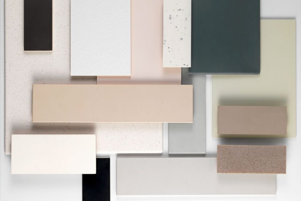 A flat-lay arrangement of various rectangular and square material samples in muted tones, including shades of cream, beige, grey, and deep forest green.